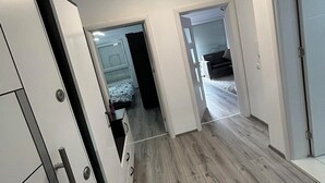 Un couloir moderne avec un plancher en bois, des murs blancs et un luminaire au plafond. On y trouve des portes donnant accès à une chambre et à une salle de bain.