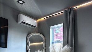 Une chambre moderne aux tons de gris, agrémentée d’un miroir ondulé original, d’une chaise noire, d’un vase contenant des plumes d’herbe des pampas et d’une fenêtre avec des rideaux.