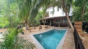 Ein rechteckiger Pool mit Holzterrasse, umgeben von Palmen und Gartenmöbeln.