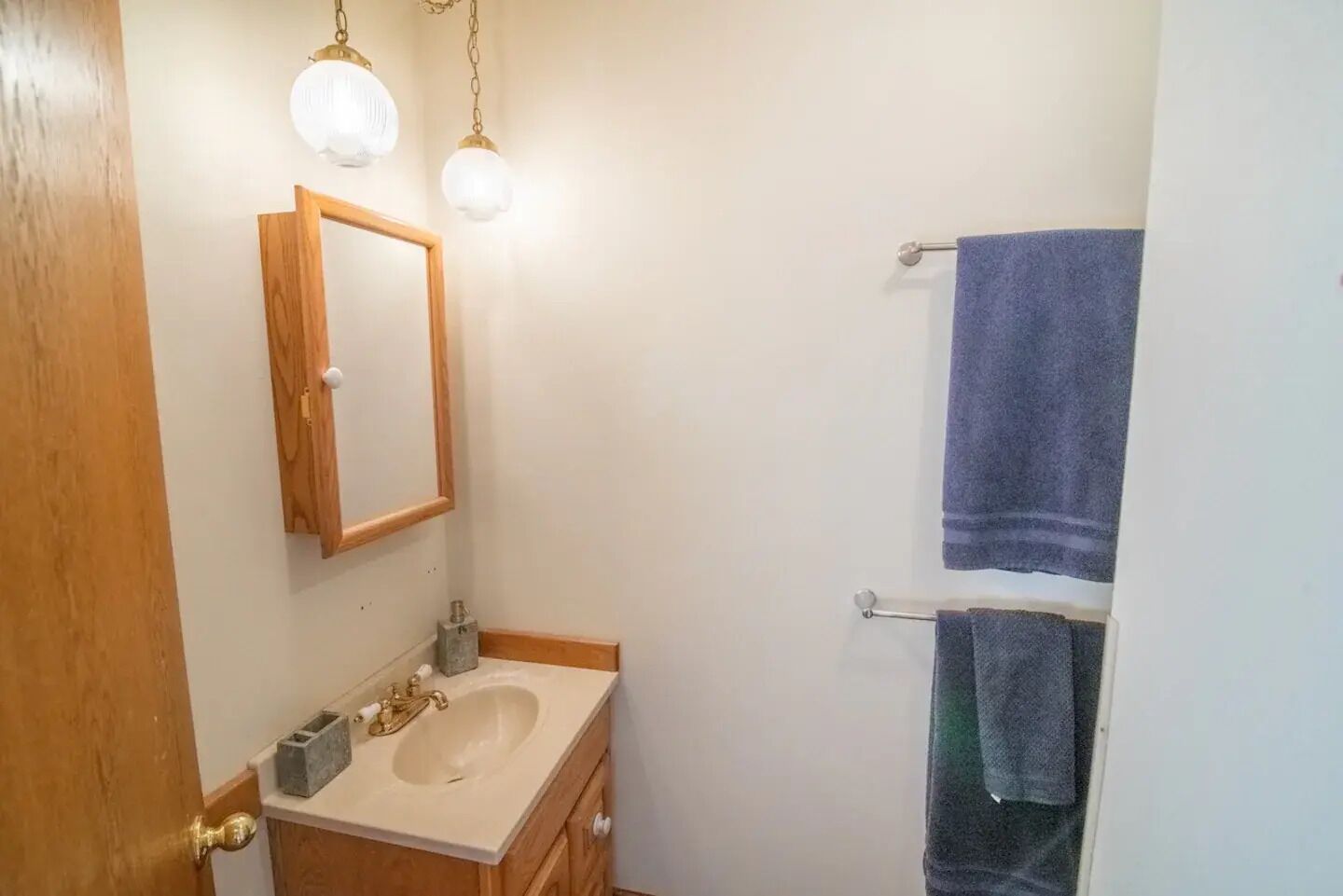 A bathroom with a wooden vanity, a mirror, a sink, and two towels hanging on a rack.