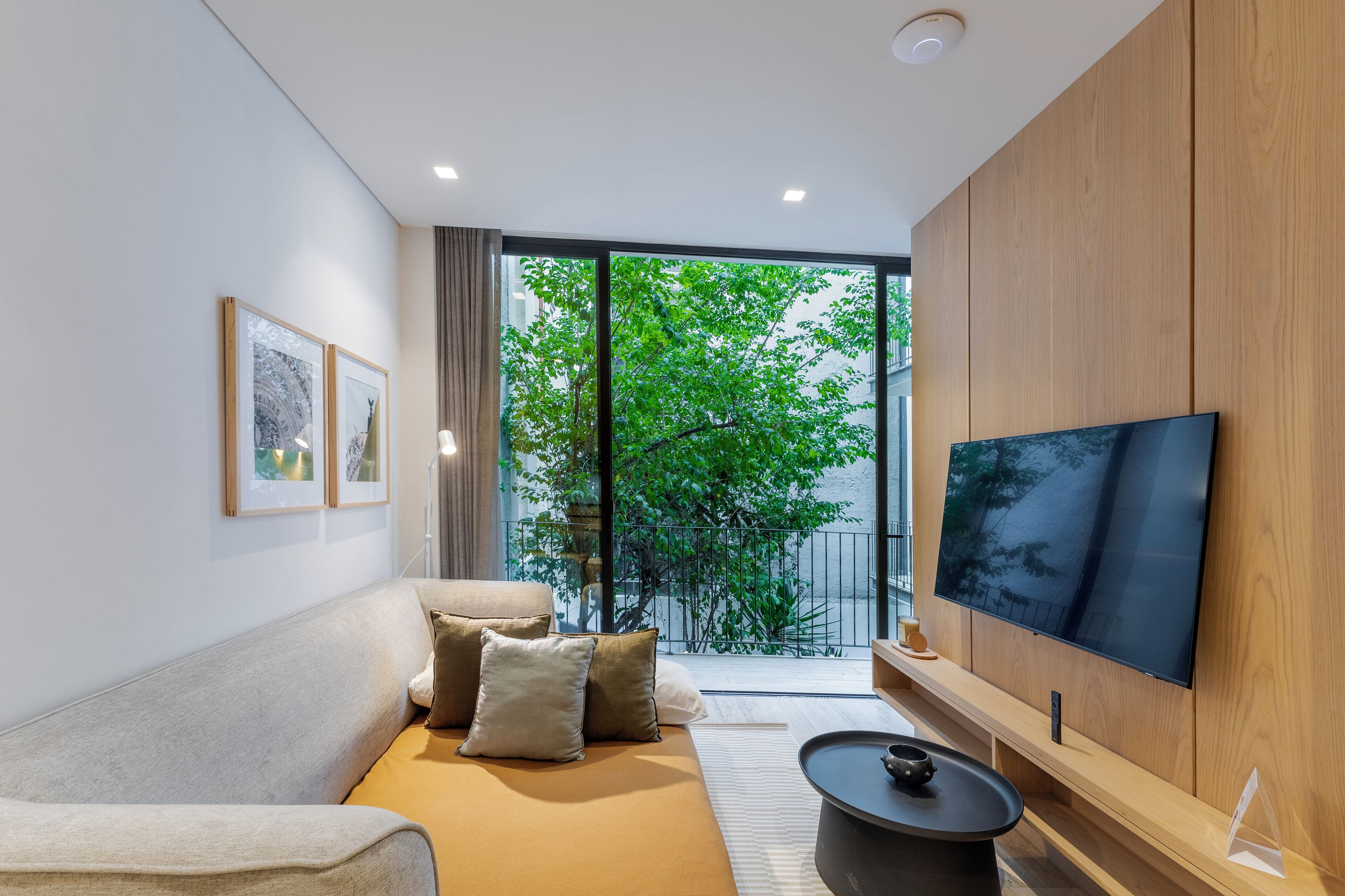 Uma sala de estar moderna com sofá, televisão de tela plana e vista para uma varanda com vegetação.
