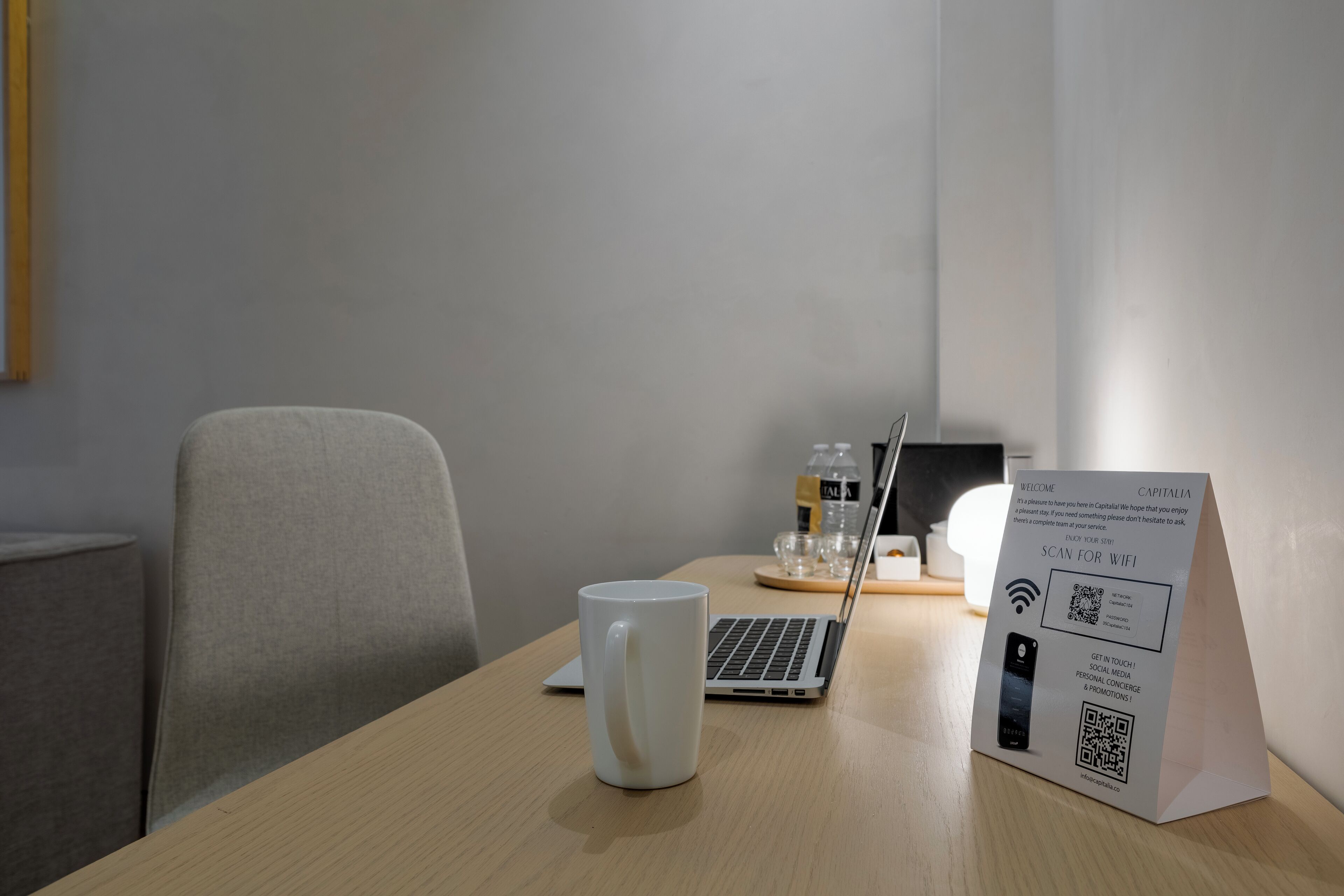 A hotel room with a wooden desk, a laptop, a white mug, and a sign promoting WiFi and mobile connectivity.