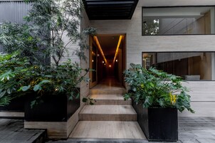 Una entrada moderna a un edificio con una escalera de madera que conduce a un interior bien iluminado.