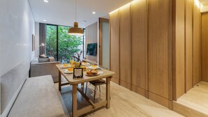 A modern dining area with a wooden table, bench seating, and a view of greenery outside.