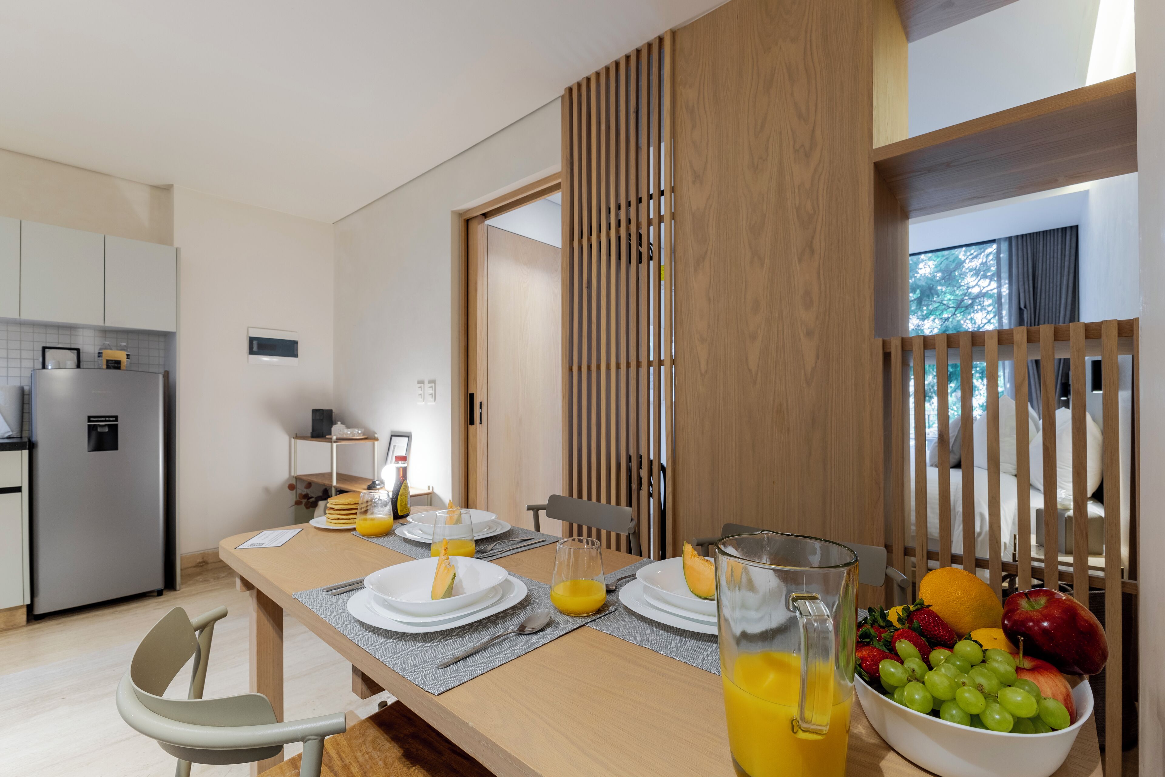 Une cuisine moderne avec un coin repas, comprenant une table en bois dressée pour le petit-déjeuner, avec des assiettes, des verres et un saladier de fruits.