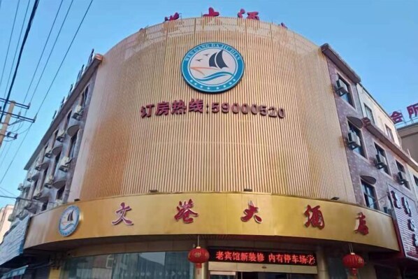 A building with a circular facade, a logo at the top, and a sign with Chinese characters. - Shipu Wengang Hotel (Xiangshan)