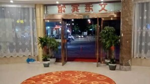 L’entrée d’un hôtel, avec un tapis rouge, des plantes en pot et une enseigne au-dessus des portes.