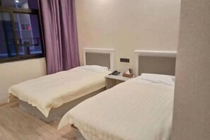 A hotel room with two single beds, a window with purple curtains, and a bedside table with a phone and tissues.