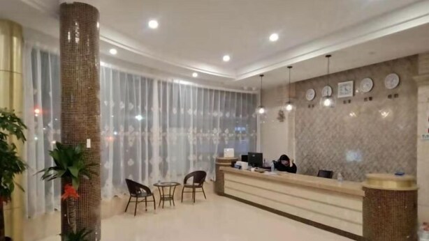 Un espace d’accueil d’hôtel comprenant un comptoir de réception, des chaises et des plantes en pot.
