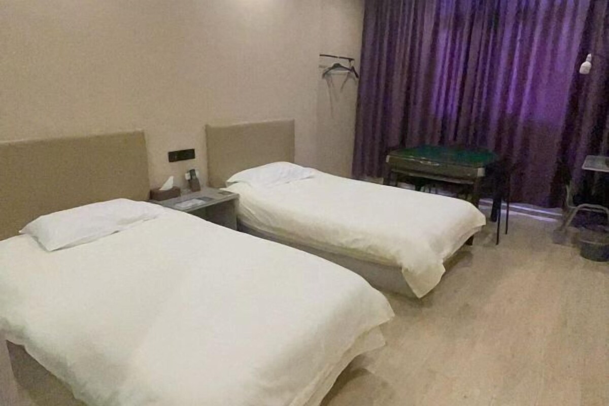 A hotel room with two single beds, a small table, a chair, a desk, and a curtain.