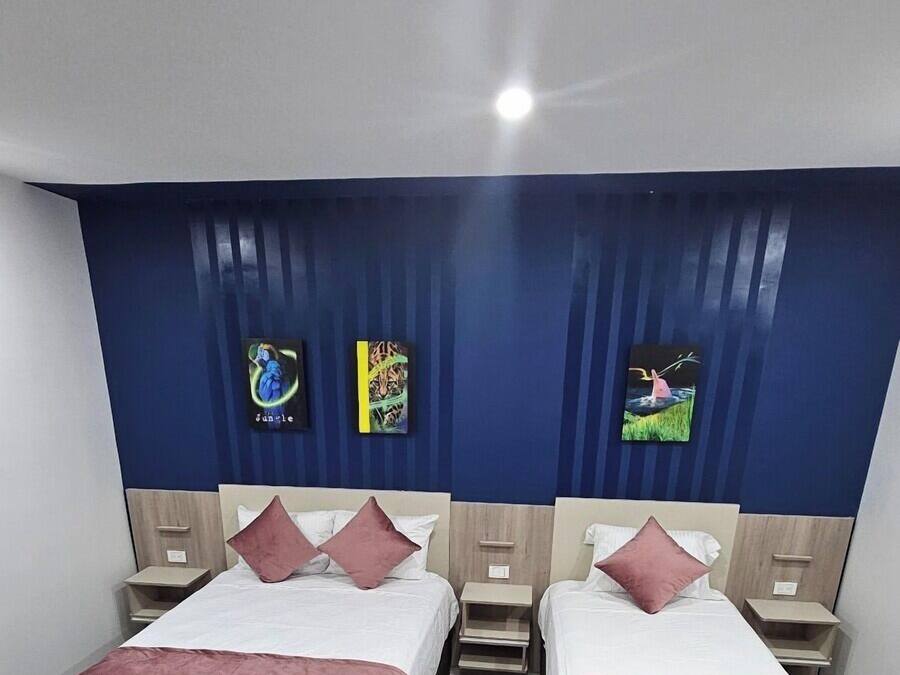 A hotel room with two beds, each with a wooden frame and a red bedspread. There are two nightstands with lamps, and a blue curtain with vertical stripes.