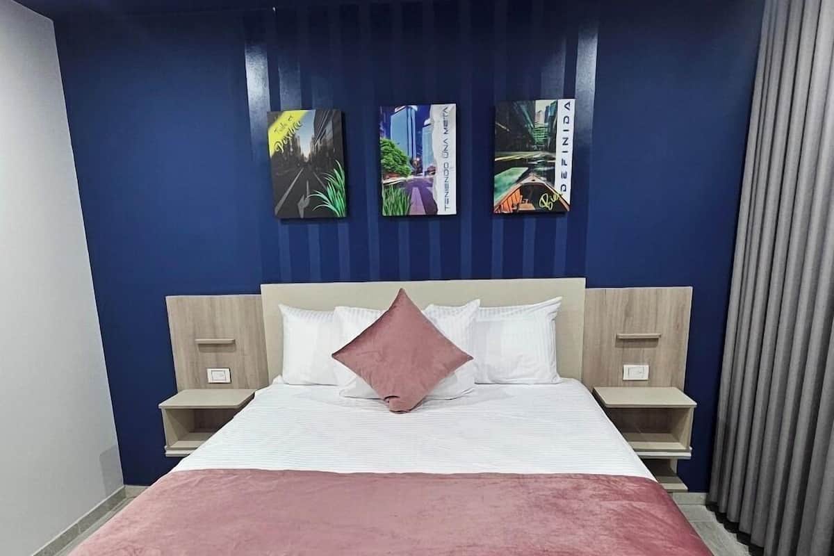 Une chambre d’hôtel moderne avec un grand lit, deux tables de chevet et une tête de lit dotée d’un éclairage intégré.