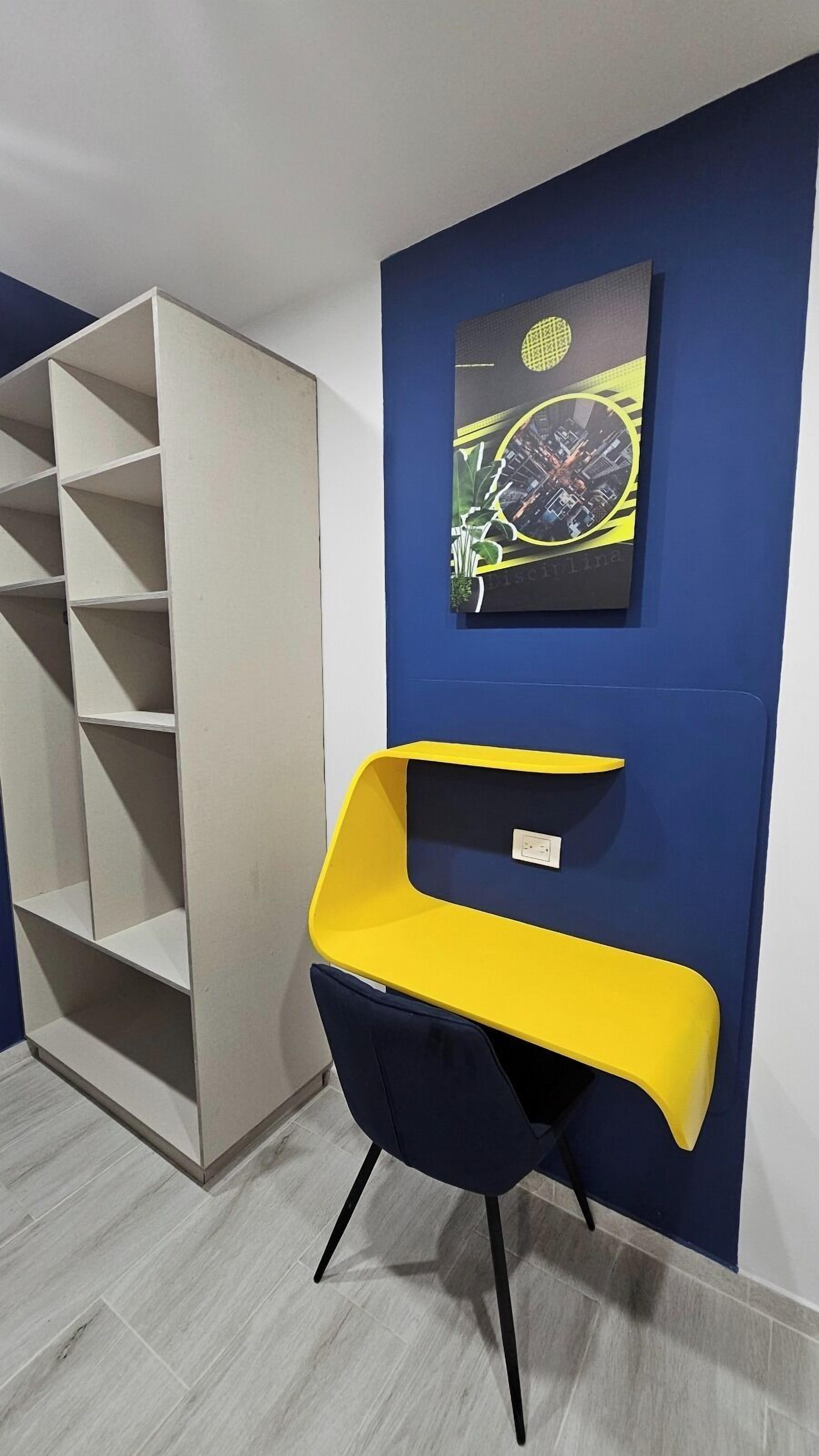Een kamer met een blauwe wand, een wit dressoir, een gele stoel en een lijst met een foto.