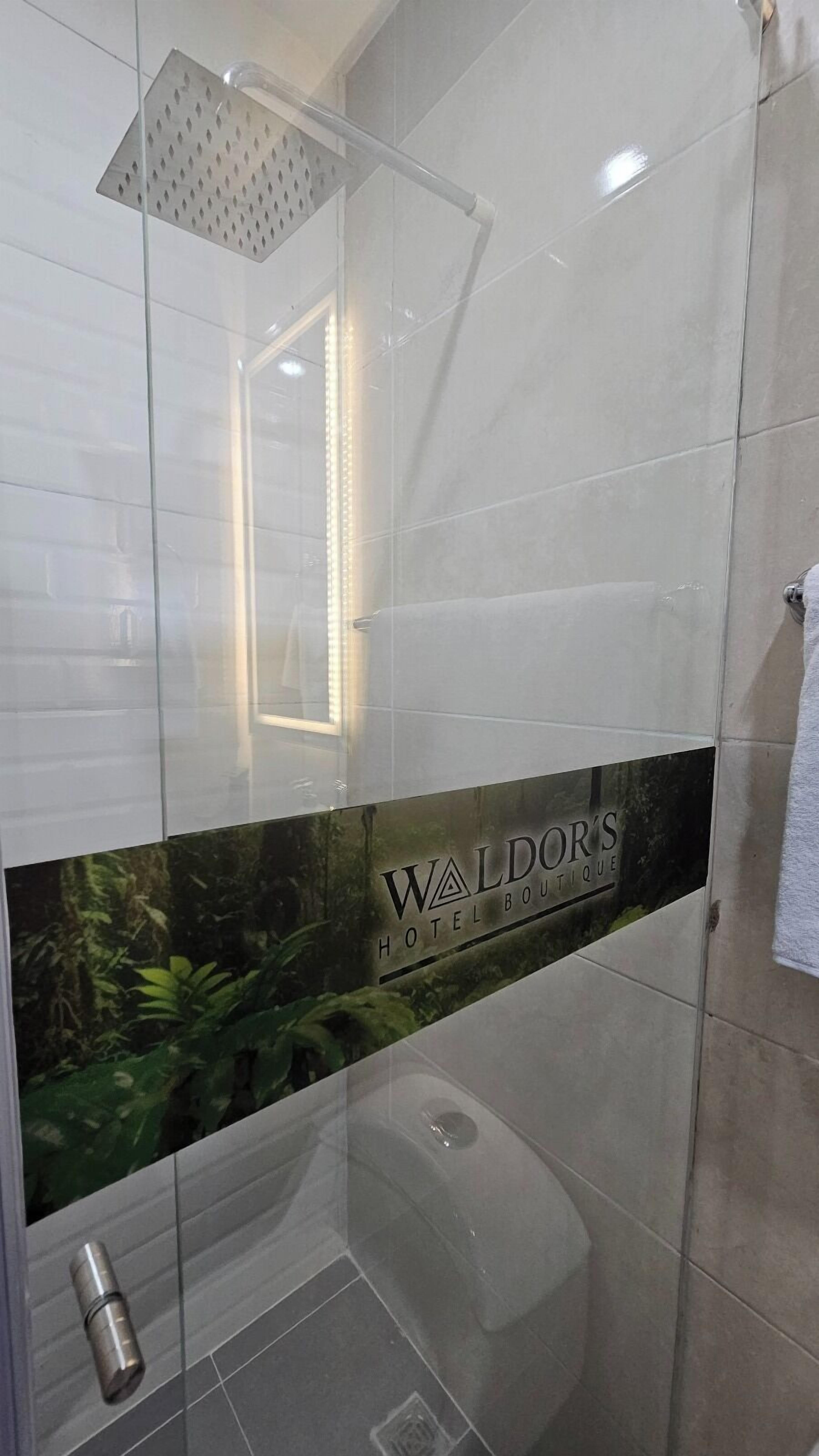 Ein modernes Badezimmer mit Duschkabine aus Glas, einer sichtbaren Toilette und einer Dekoration mit dem Text "Waldor's Hotel Boutique".