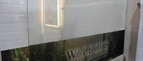 Ein modernes Badezimmer mit Duschkabine aus Glas, einer sichtbaren Toilette und einer Dekoration mit dem Text "Waldor's Hotel Boutique".