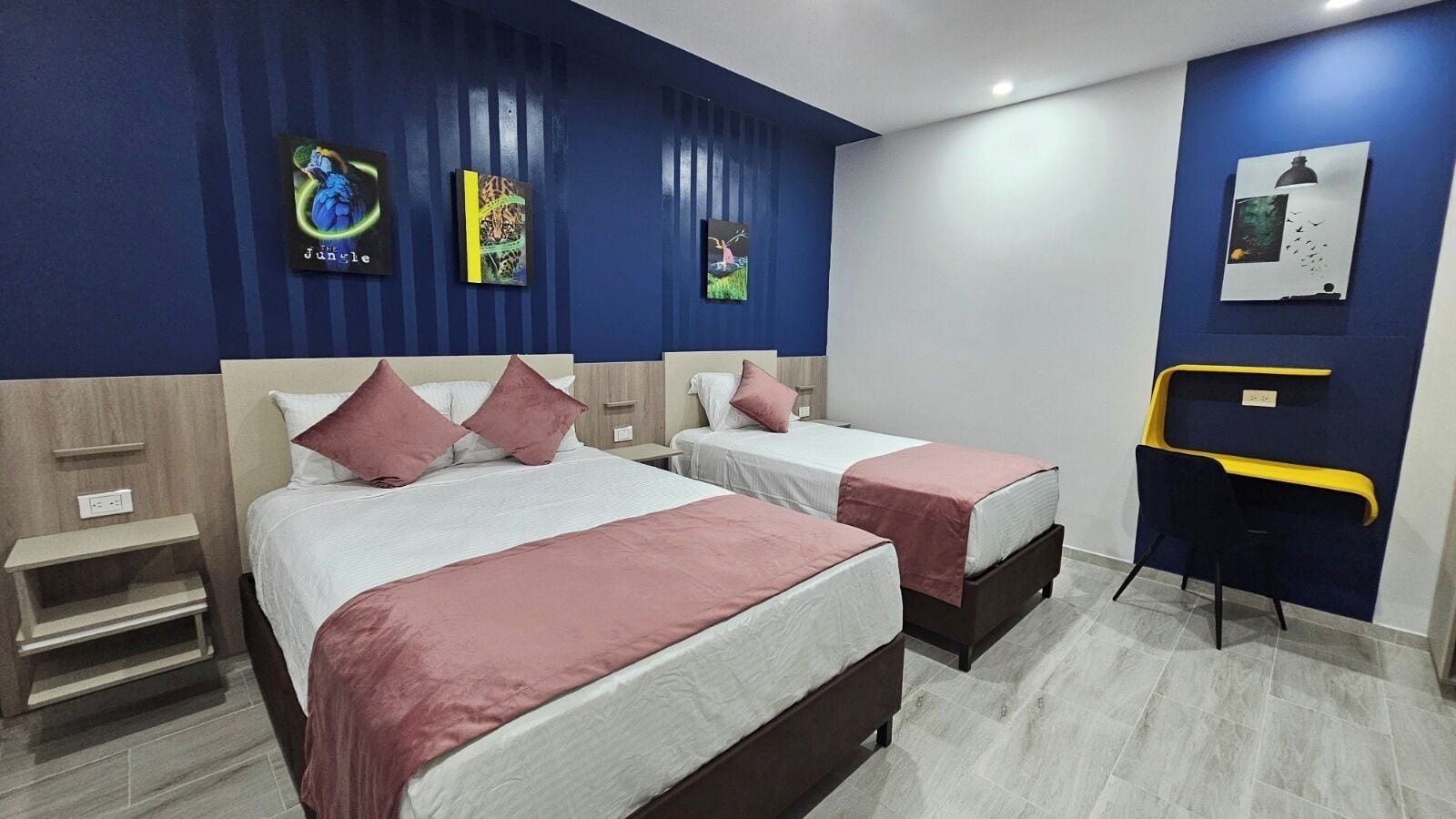 A hotel room with two beds, a desk, and artwork on the walls.