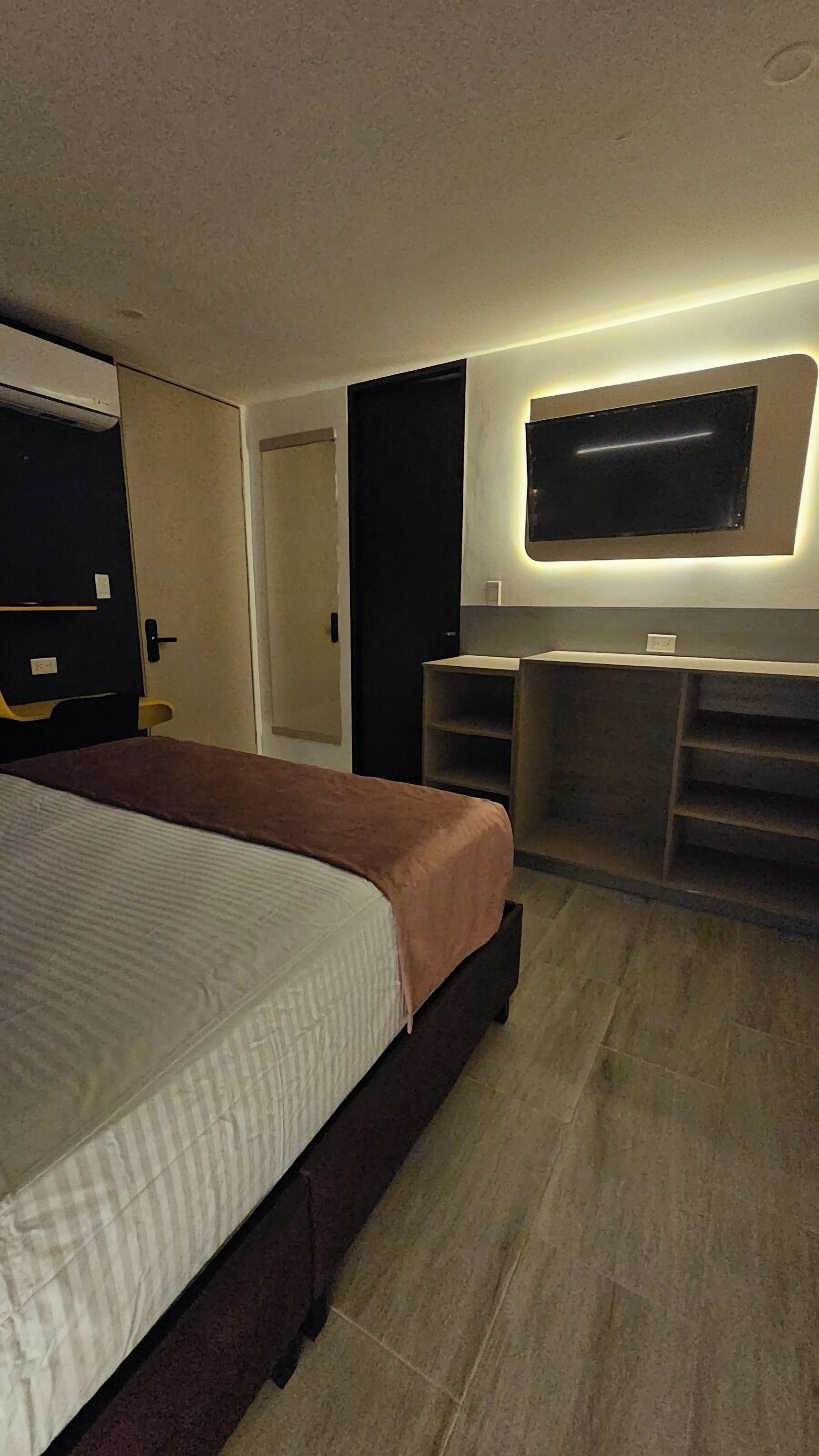 A hotel room with a bed, a desk, a chair, a television mounted on the wall, and a door.