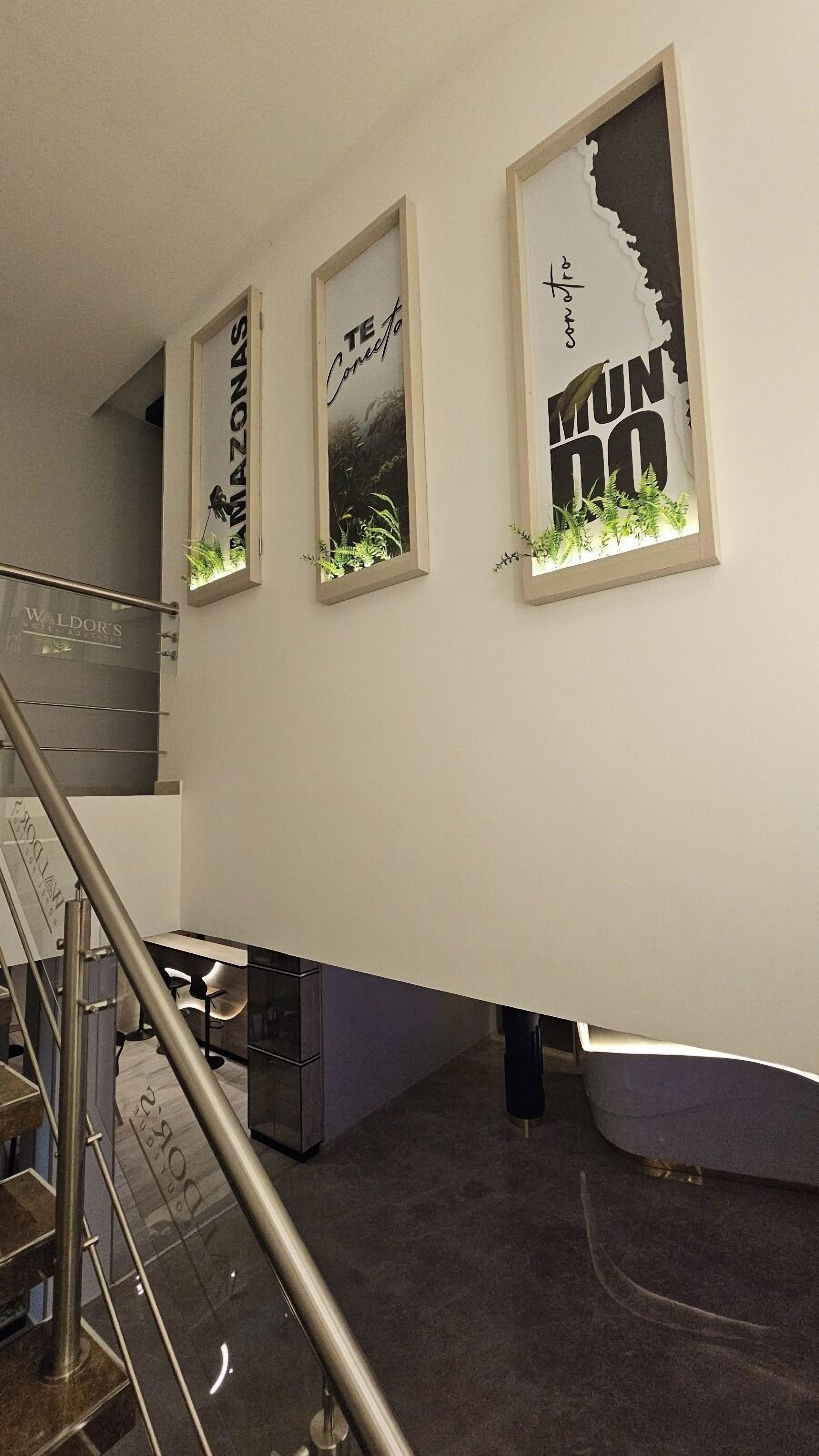 A staircase with a metal railing leading to a landing. On the landing, there are three framed artworks with text and images of plants.