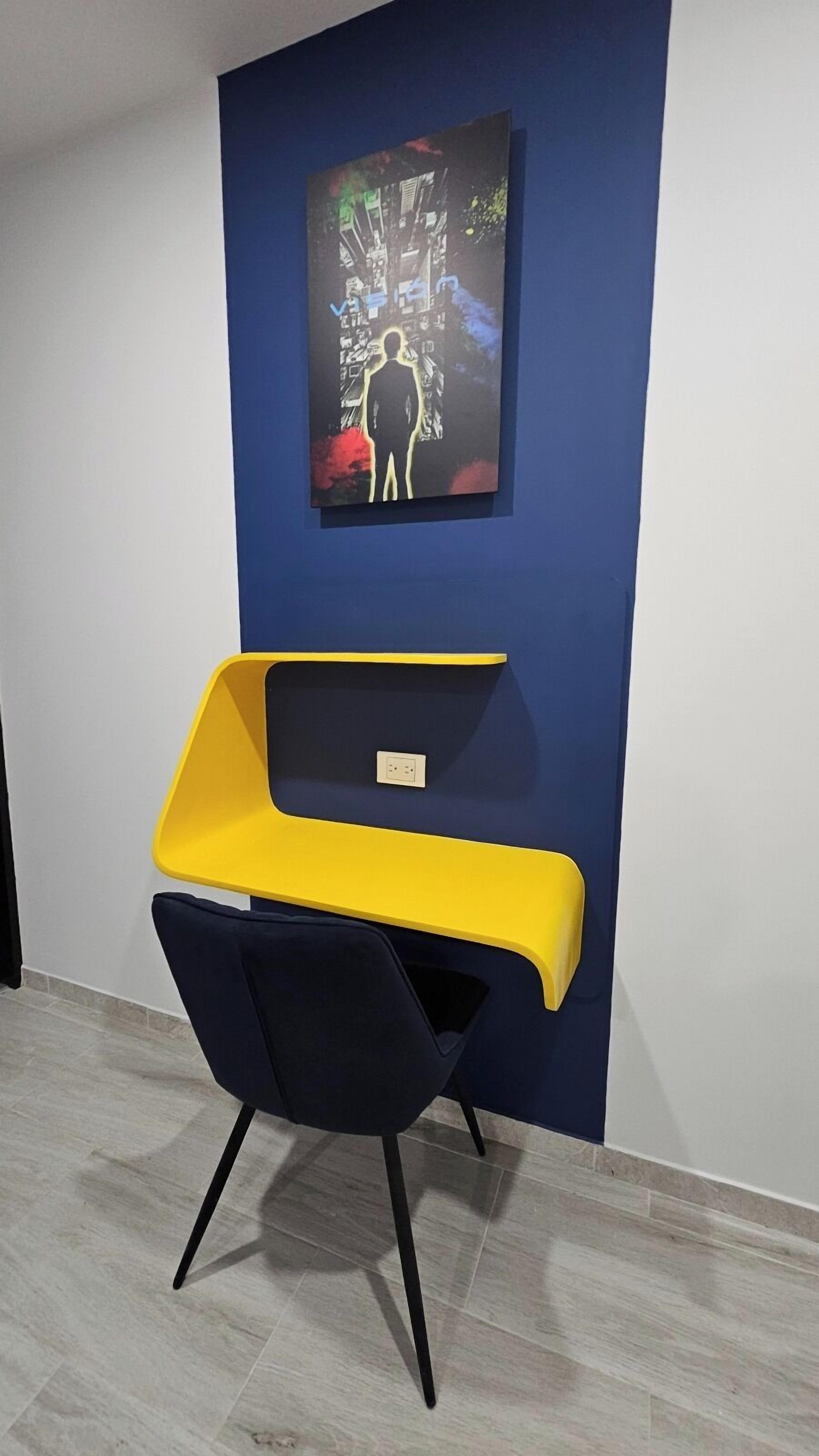 Een moderne kamer met een blauwe accentmuur, een gele en zwarte stoel en een schilderij van een persoon voor een boom.