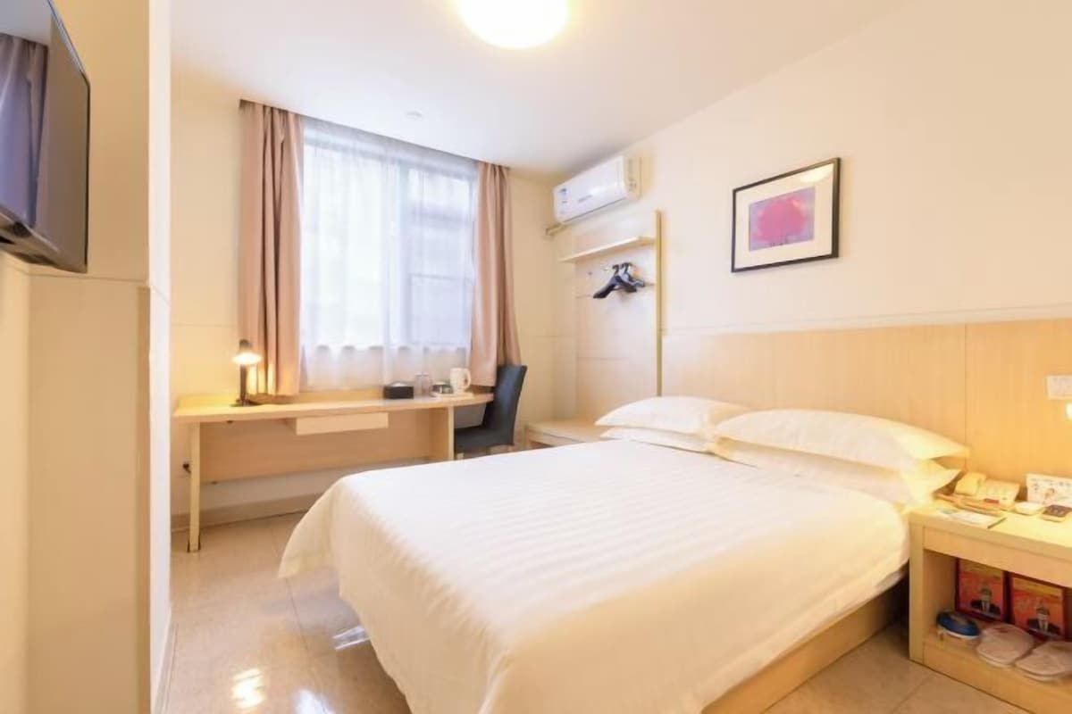 A hotel room with a bed, desk, chair, and a window with curtains.