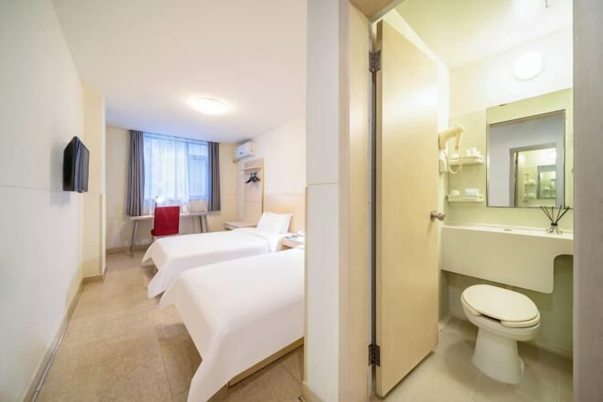 A hotel room with two beds, a desk, a chair, a TV, a bathroom with a toilet and sink.