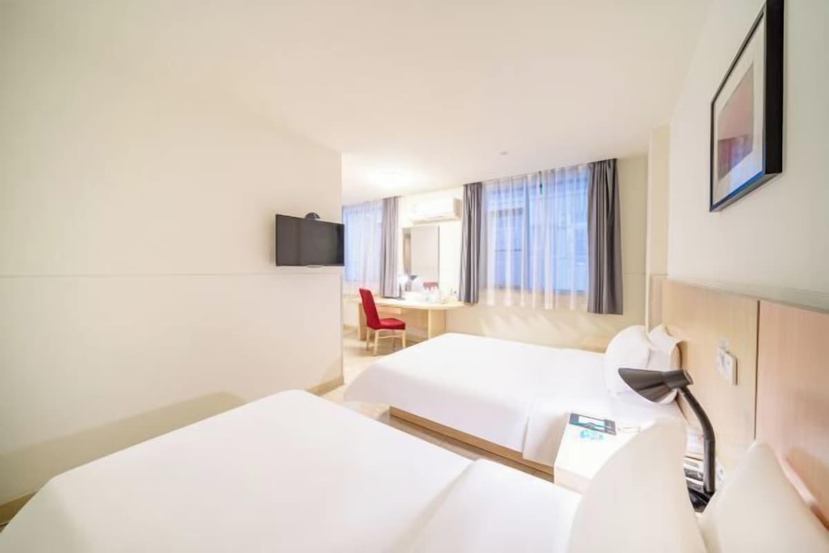 A hotel room with two beds, a desk, a chair, a TV, and a window with curtains.