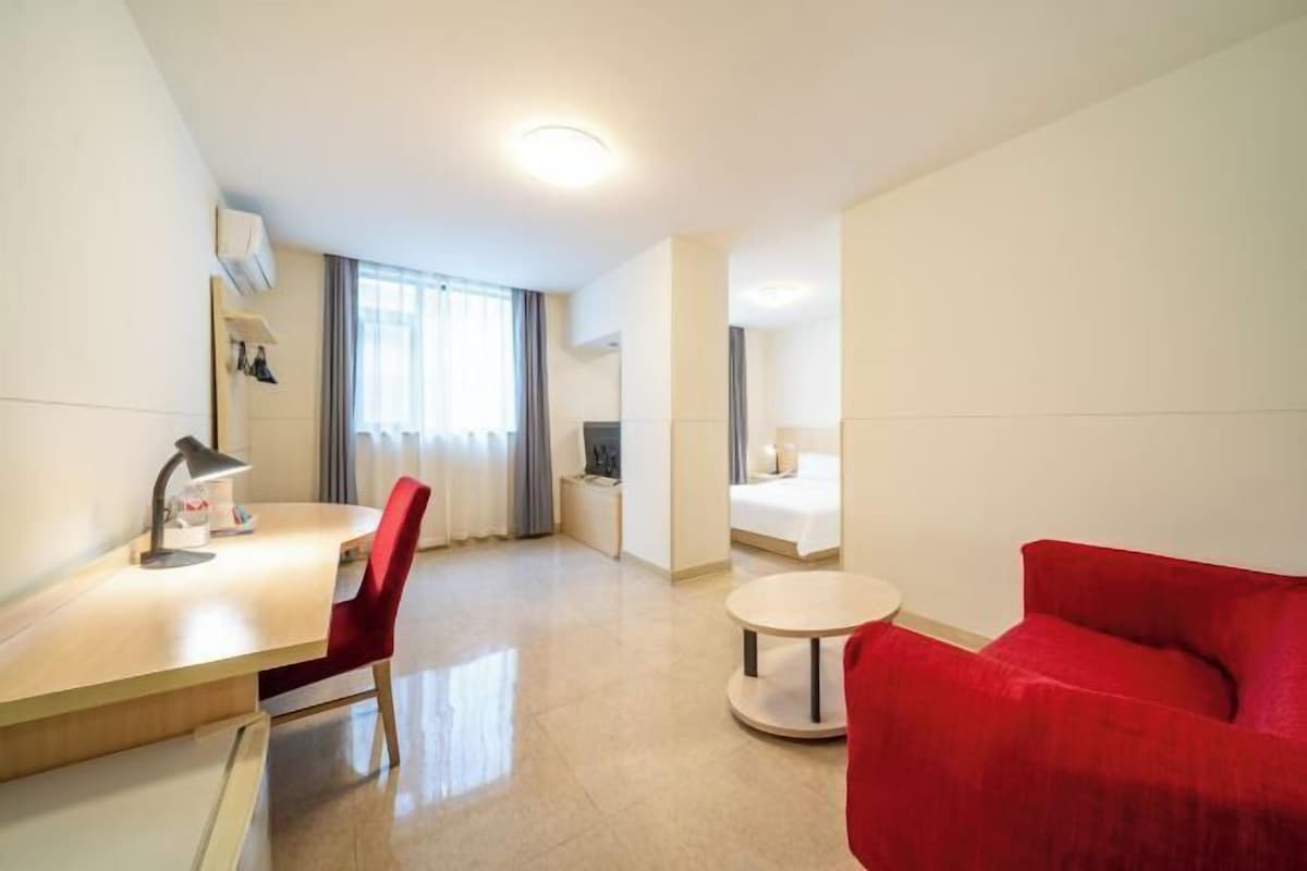 A hotel room with a desk, chair, red sofa, round table, and a bed.