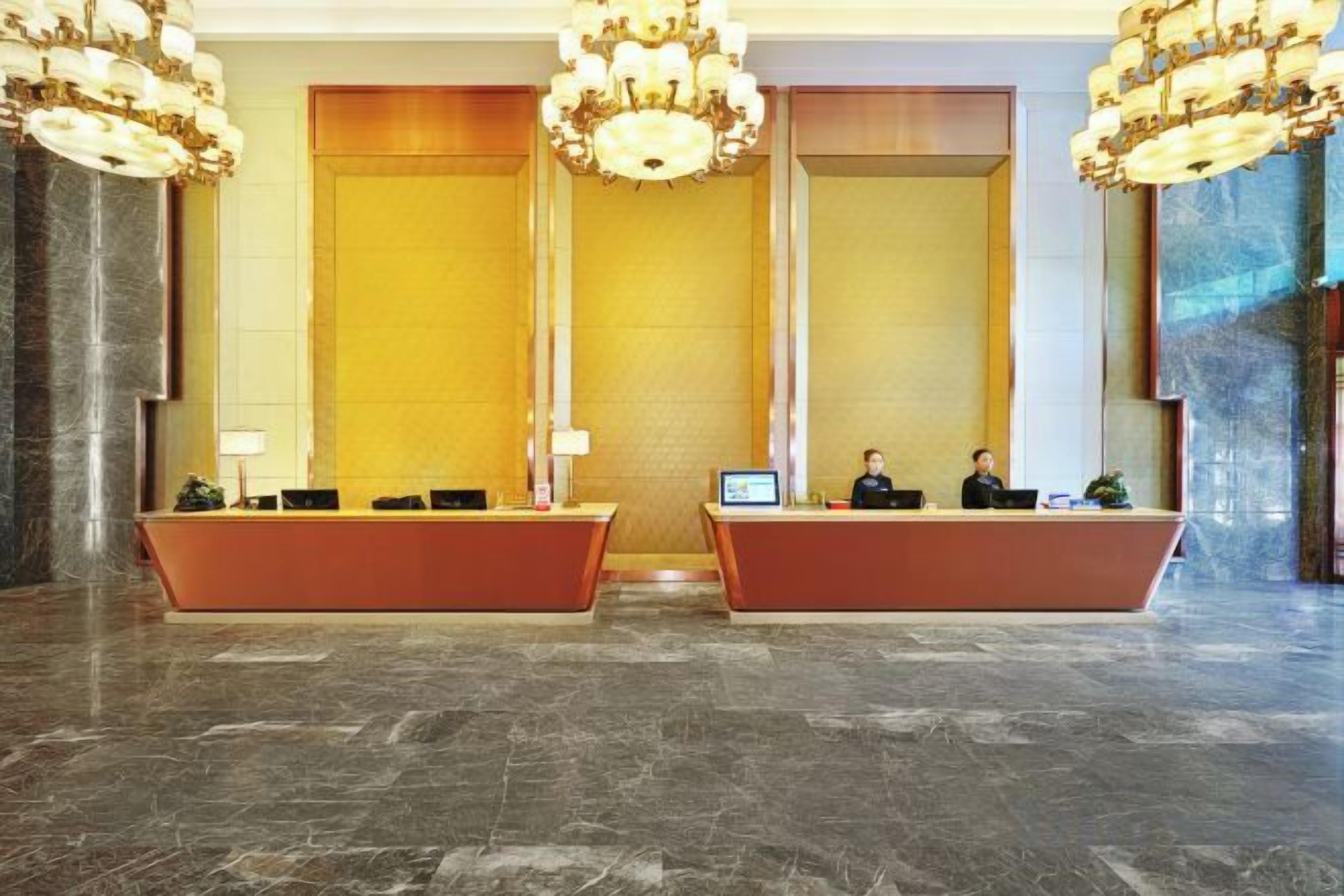 A hotel reception area with two reception desks, a large chandelier, and a marble floor.