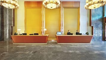 A hotel reception area with two reception desks, a large chandelier, and a marble floor.