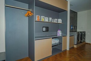 Zona de lavandería con lavadora, secadora y estantes con ropa doblada y útiles de limpieza.