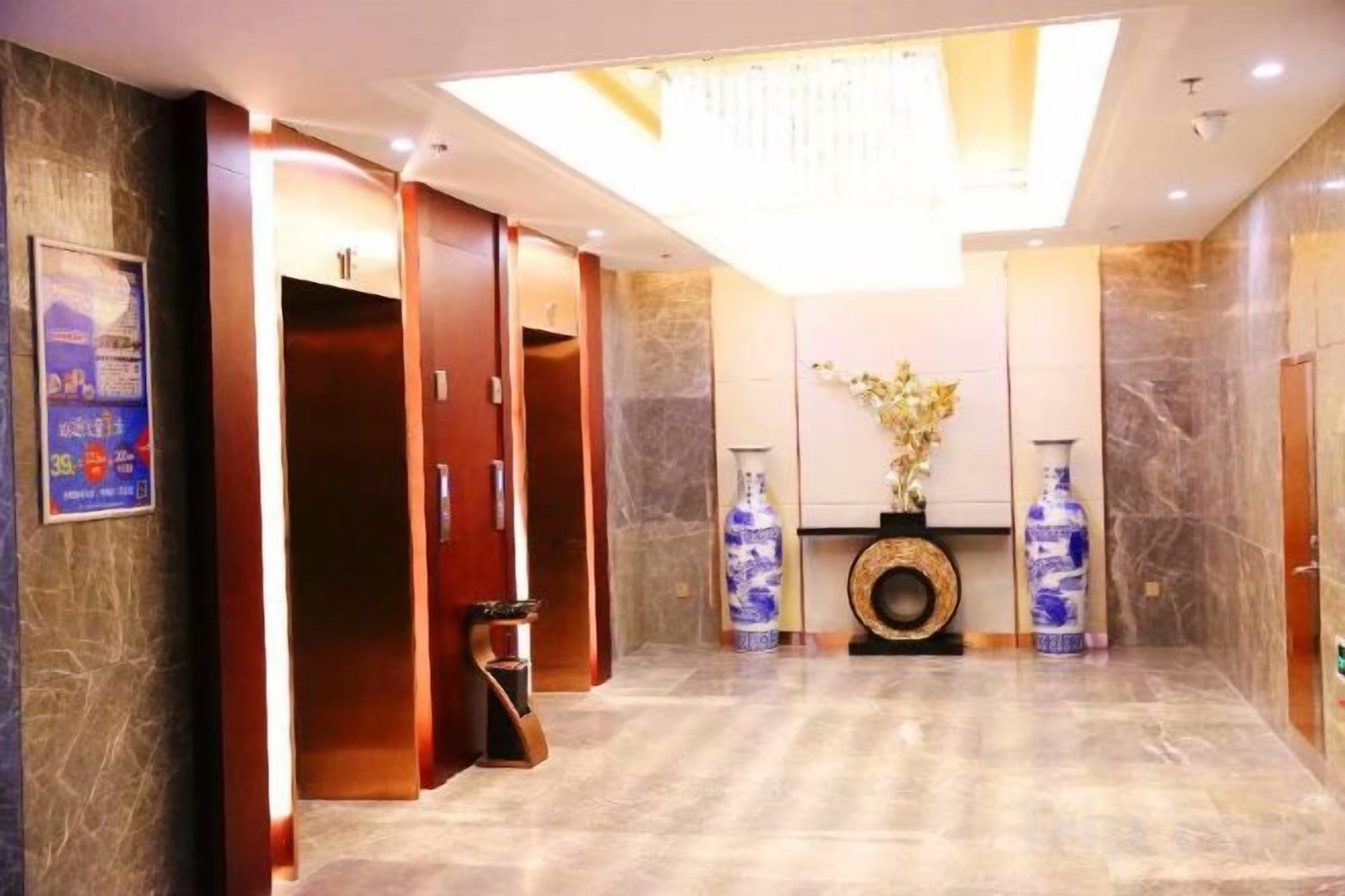 A hotel lobby with a reception desk, a large vase with flowers, and a wall-mounted clock.