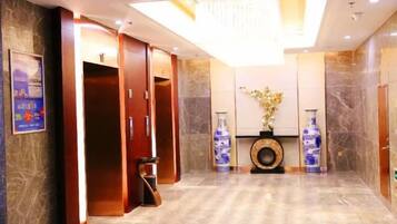 A hotel lobby with a reception desk, a large vase with flowers, and a wall-mounted clock.