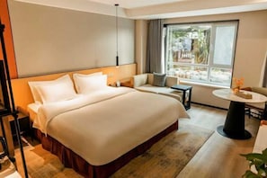 Quarto de hotel com uma cama grande, um sofá, uma mesa pequena e janela com vista para o exterior.