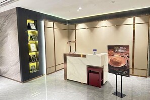 Un área de recepción con un mostrador de mármol, un pequeño bote de basura rojo y un expositor de información adosado a la pared.