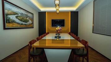 A conference room with a long table, chairs, a chandelier, a painting, and a television screen.