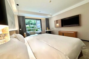 Quarto de hotel com duas camas, televisão na parede, janela com cortinas e uma pequena mesa com abajur.