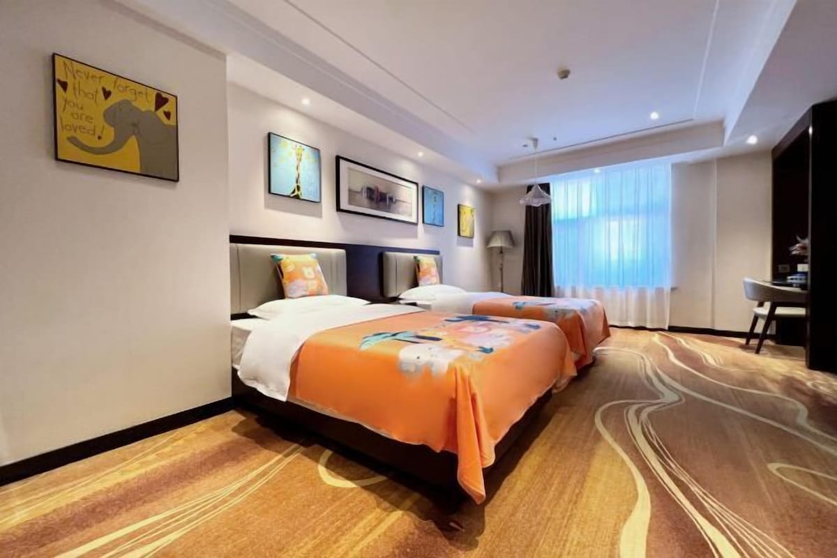 Quarto de hotel com duas camas, uma escrivaninha e uma janela grande com cortinas.