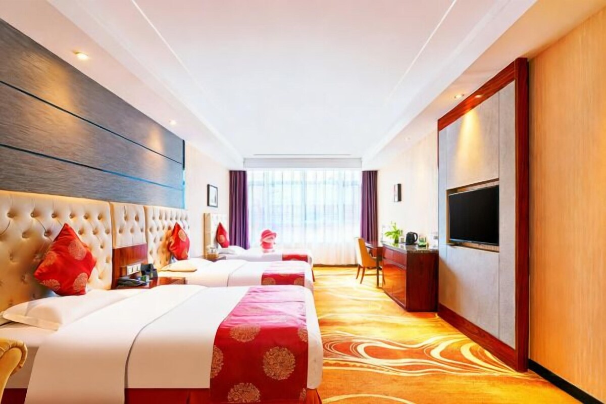 Quarto de hotel com duas camas, televisão, escrivaninha e uma janela grande.
