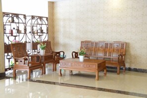 A traditional wooden sofa set with a matching coffee table, a wooden cabinet, and a decorative screen in a well-lit room with a patterned wall. - E·E Business Hotel (Guangzhou)