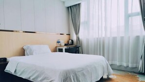 Une chambre d’hôtel avec un lit, une table de chevet, une petite table avec une lampe et une fenêtre avec des rideaux.