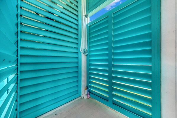 Una esquina de una habitación con contraventanas color turquesa, un tubo blanco y una pequeña botella en el suelo.