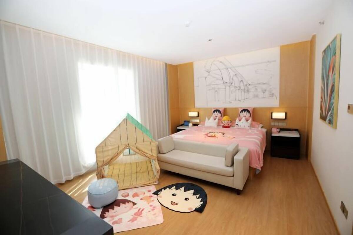 Une chambre d’hôtel avec un lit, des lampes de chevet, une petite maison de jeu et un tapis orné d’un personnage de dessin animé.