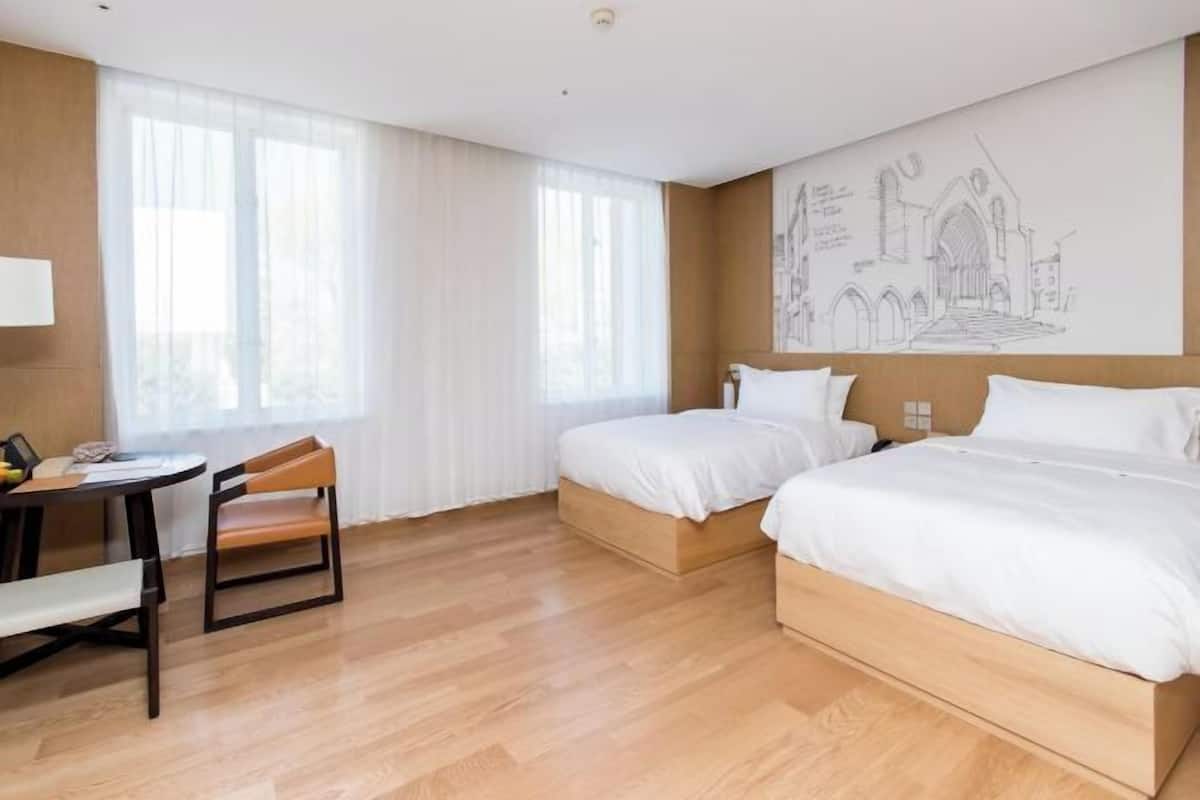 Une chambre d’hôtel avec deux lits, un bureau, une chaise et de grandes fenêtres.