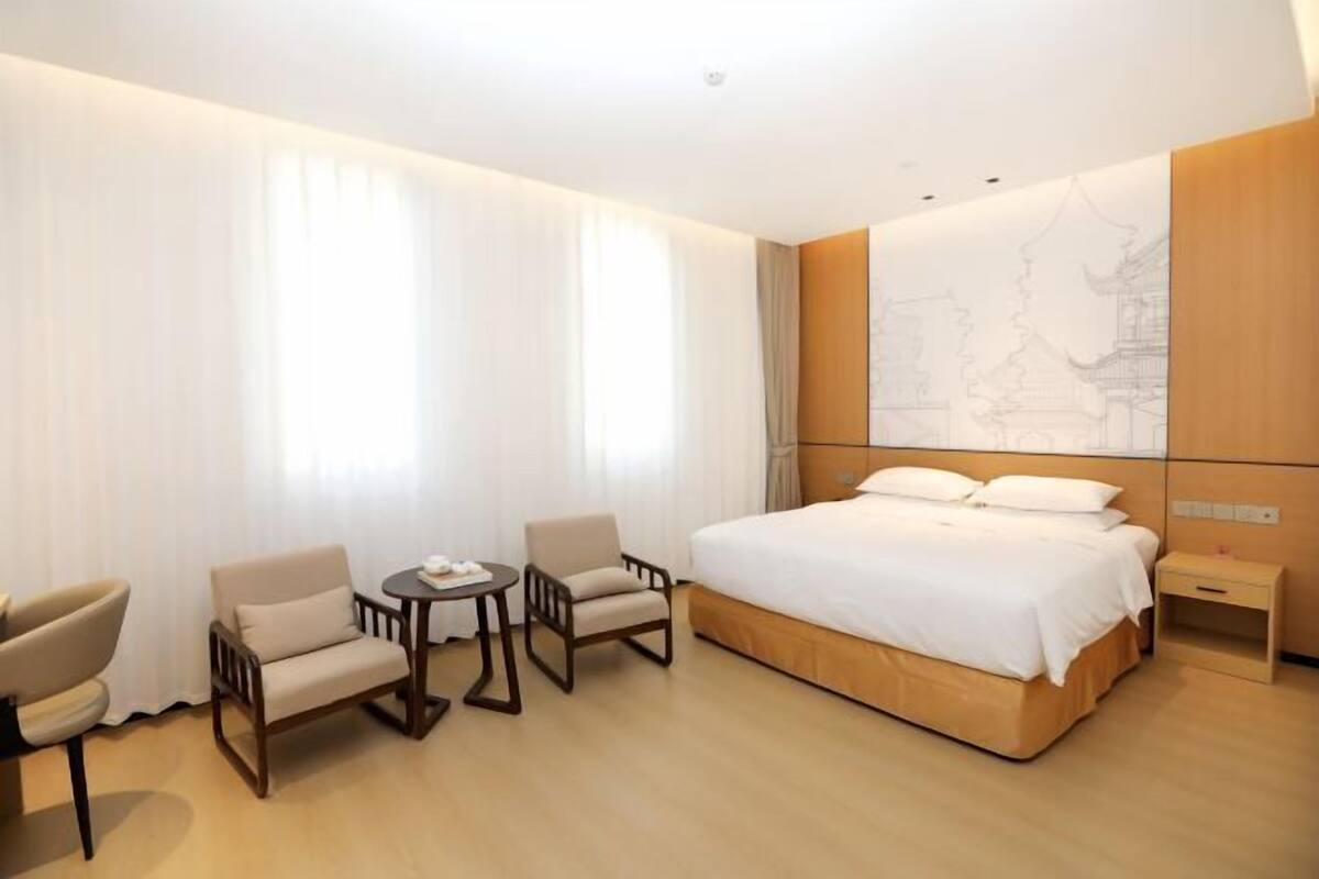 Une chambre d’hôtel avec un grand lit, deux fauteuils, une petite table et une table de chevet.