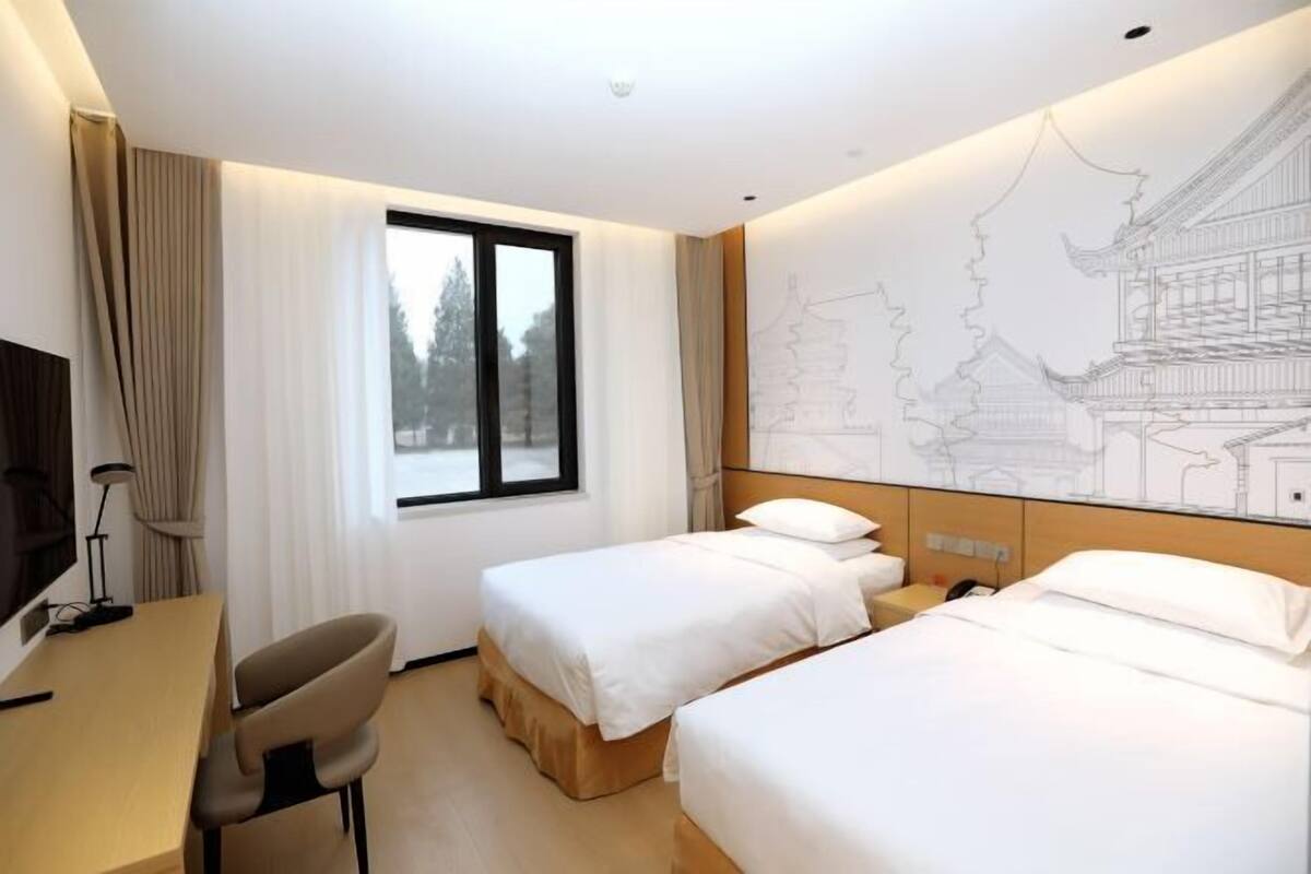 Une chambre d’hôtel avec deux lits, un bureau, une chaise et une grande fenêtre.