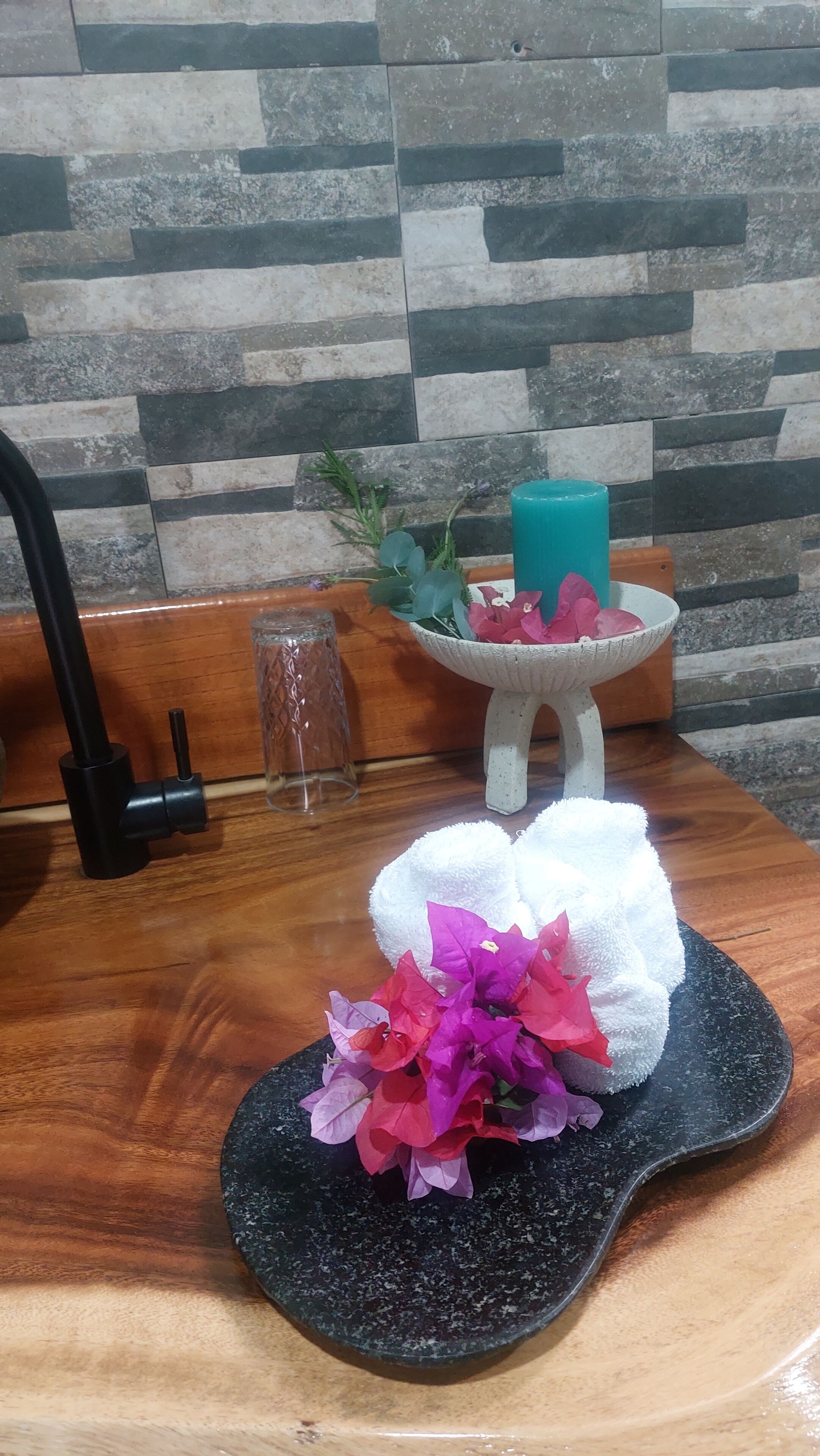 Ein Badezimmer mit einem Holzbadezimmerhocker, einem schwarzen Granittischwaschbecken, einem weißen Handtuch und einer Blumenstilllegung.