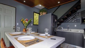 A modern kitchen with grey cabinets, a white island, and a dining area set for four with a vase of flowers. - Charming 2-bedroom villa surrounded by nature in phenomenal Monteverde with WiFi (Monteverde)