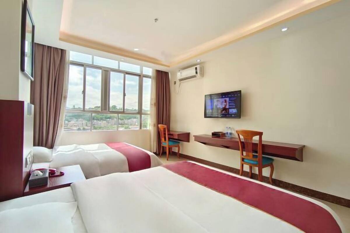 Een hotelkamer met twee bedden, een bureau, een televisie en een raam met uitzicht over de stad.