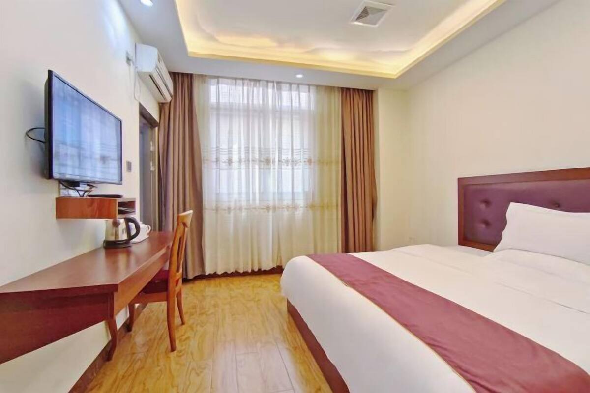 Een hotelkamer met een bed, een bureau met stoel, een televisie en een raam met gordijnen.