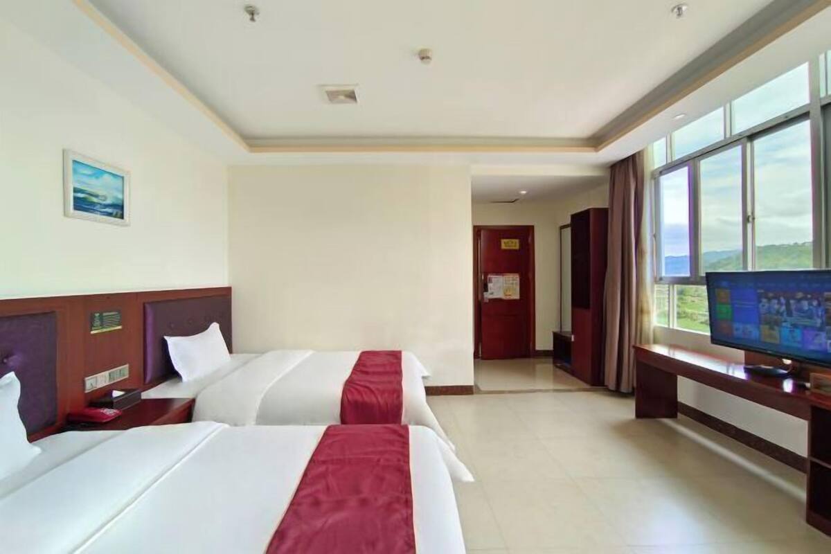 Een hotelkamer met twee bedden, een televisie en een groot raam.